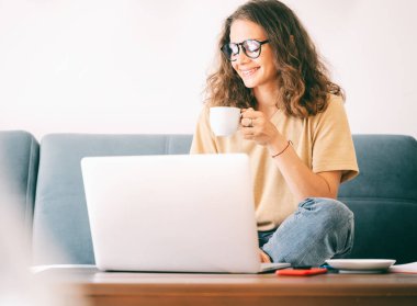 Genç, güzel, kıvırcık bir kadın. Gözlüklü. Sabah kahvesinin keyfini çıkarıyor..