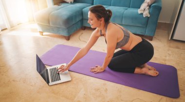 Spor giyimli bir kadın evde oturma odasında dizüstü bilgisayar kullanarak yerde oturuyor. Spor ve eğlence konsepti.