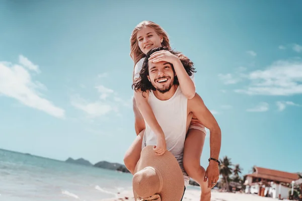 ビーチでの夏休みには幸せなカップル ブロンド女の子Piggybackingオン若いですブラジルのボーイフレンド遊びと楽しみますで日当たりの良い熱帯目的地 — ストック写真