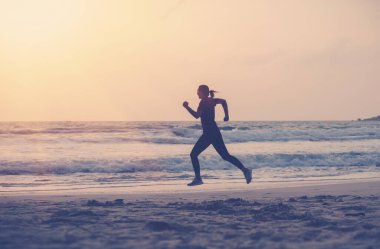 Spor üniformalı bir kadın şafak vakti okyanus kıyısında koşuyor, koşuyor ve sağlıklı yaşam tarzını sürdürüyor.