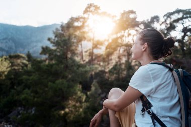 Sırt çantalı güzel bir kız. Ormanın ve doğanın tadını çıkarıyor. Gün batımında ormanda yürüyor.