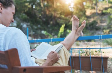 Ormana bakan kır evinin terasında kitap okuyan mutlu genç bir kadın..