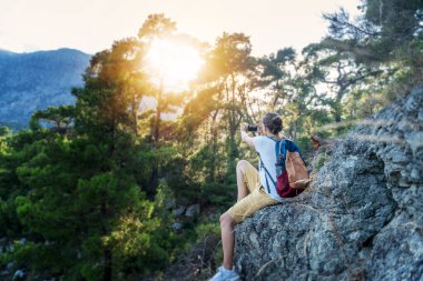 Genç kadın gezgin, ormanda yürürken, doğa ve yalnızlığın, seyahatin ve yaz maceralarının tadını çıkarırken akıllı telefonuyla fotoğraf çekiyor..