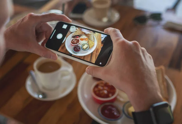 Photo of food on a smartphone in a cafe, male hands take a picture of a breakfast of scrambled eggs.