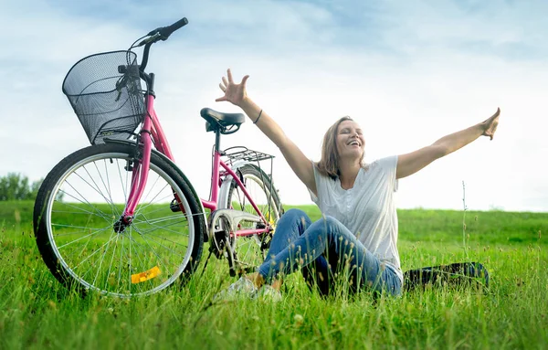 幸せな女性は自転車の横にある緑の牧草地に草の上に座って 手を上げて 夏休みと冒険のコンセプト — ストック写真