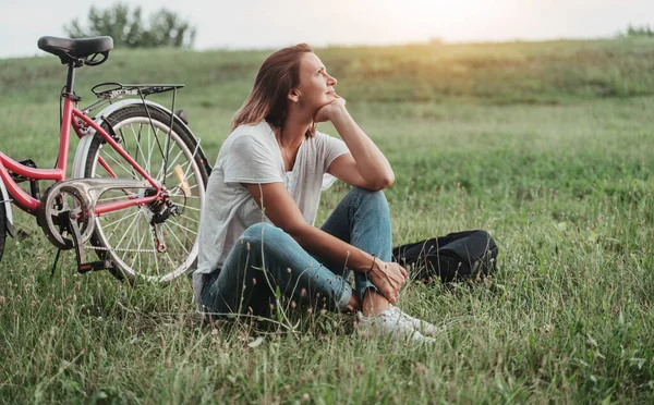 美しい笑みを浮かべて成熟した女性は緑のフィールド上の芝生の上で自転車の横に座っている 夏の国の休暇とアドベンチャーコンセプト — ストック写真