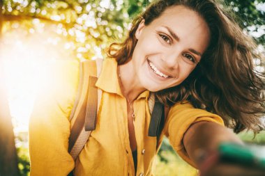 Güneşli bir yaz parkında, yüzünde ve kafasında sarı gömleğiyle büyüleyici bir tebessümle güzel, genç bir kadın.