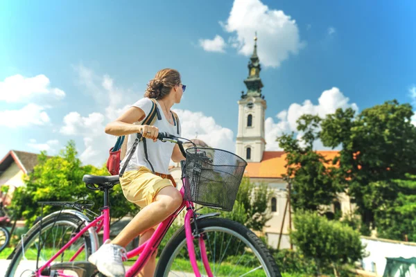若い美しいスタイリッシュな女の子はセルビアで自転車で移動します 古刹を背景に立つ — ストック写真