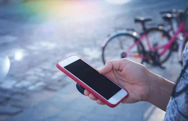 Smartphone in a womans hand on the street in a European city, bike rental in the city mobile app concept — Stock Photo, Image