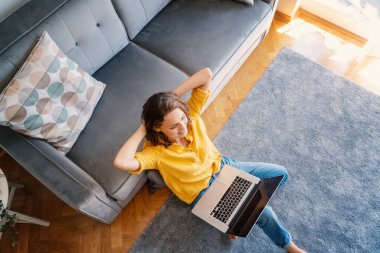 Sarı tişörtlü güzel bir kız evde dizüstü bilgisayarla çalışıyor oturma odasında yerde oturuyor, en iyi görüntü.