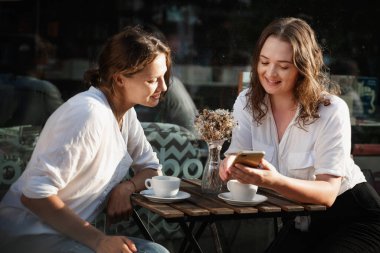 İki genç bayan bir kafede kahve içerken akıllı telefon kullanıyor..