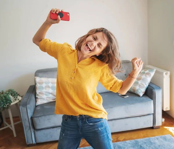 Красивая Молодая Женщина Желтой Рубашке Танцует Счастливой Радостной Гостиной Смартфоном — стоковое фото