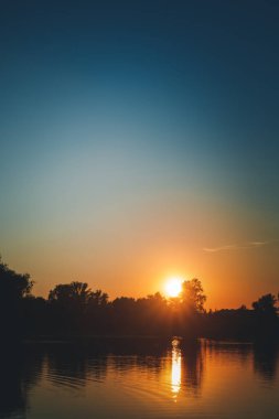Güzel yaz sonbahar manzarası, ormandaki güneş batışı, ağaçların ve çimen göletinin manzarası, suya yansıyor. Göz kamaştırıcı parlak gün batımı.