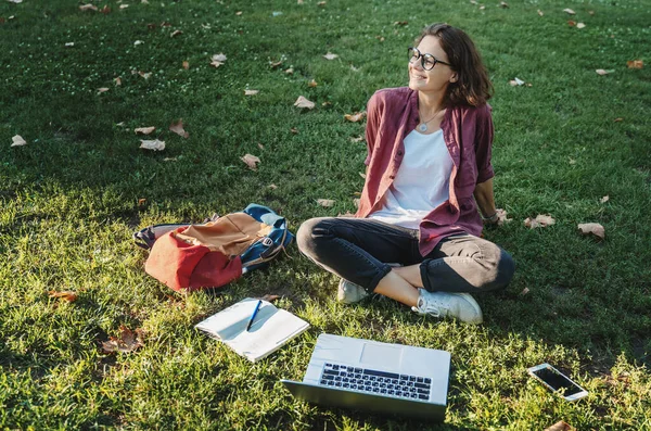 年轻的女商人学生在公园的笔记本上工作 在阳光明媚的日子里 女自由职业者坐在草地上 用手提电脑和日记 用手机在草地上 — 图库照片