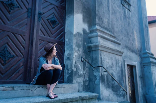 Bir ortaçağ katedralinin merdivenlerinde oturmuş Avrupa 'ya seyahat eden şapkalı güzel bir kadının portresi.