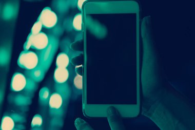 Kadın eli, arka plandaki neon ışıklarına karşı akıllı telefonu tutar, ekranı kapatır.