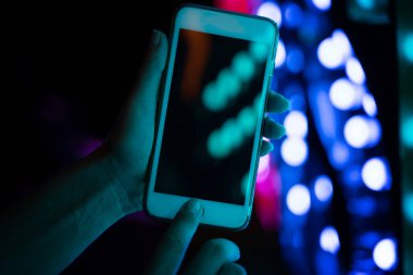 Kadın eli, arka plandaki neon ışıklarına karşı akıllı telefonu tutar, ekranı kapatır.