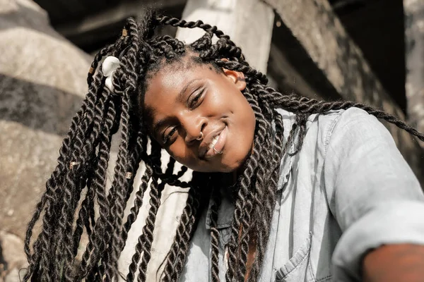 Saçları örgülü ve yüzünde piercing olan mutlu, güzel, Afro-Amerikalı bir kadın selfie yapıyor. Gülümseyen güzel bir mutluluk.