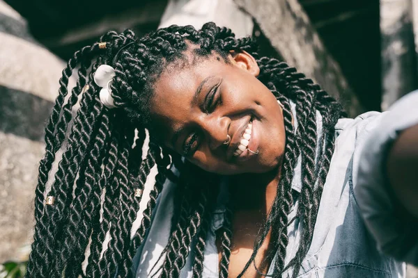 Saçları örgülü ve yüzünde piercing olan mutlu, güzel, Afro-Amerikalı bir kadın selfie yapıyor. Gülümseyen güzel bir mutluluk.