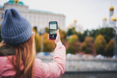 Paltolu ve şapkalı bir kadın, bulutlu bir sonbahar gününde Moskova 'nın tarihi merkezinin akıllı telefonuyla Rusya' yı geziyor.