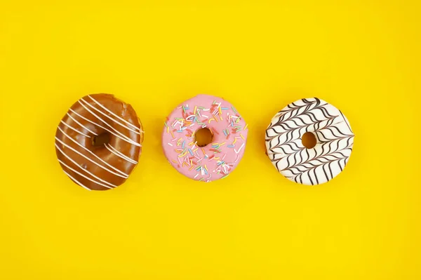 Tres rosquillas multicolores sobre fondo amarillo — Foto de Stock