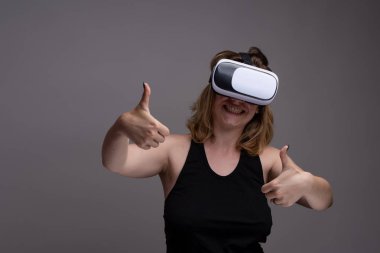 Giyilebilir 3D VR kullanan genç bir kadın iki eliyle de mutlu bir yüz ve baş parmak gösteriyor..