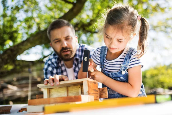 Padre con una pequeña hija afuera, haciendo pajarera de madera . — Foto de Stock