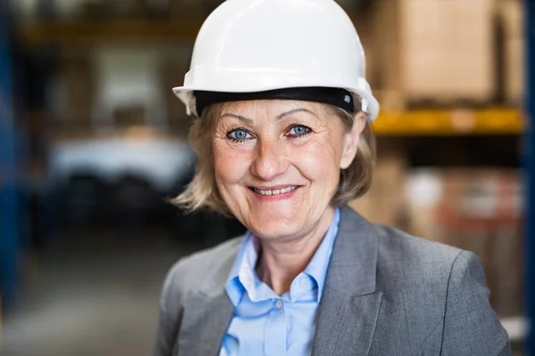 Senior vrouw magazijnbeheerder of toezichthouder met wit helm. — Stockfoto