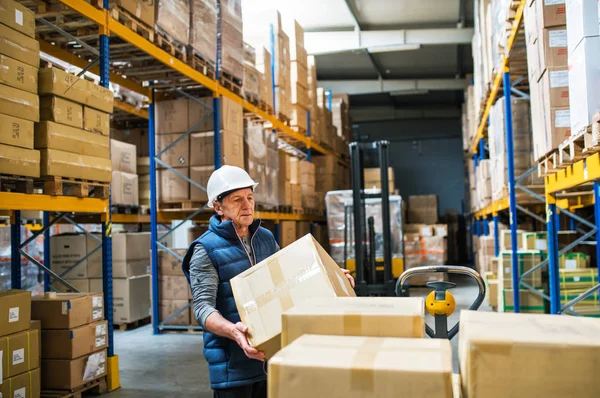 Senior mannelijke magazijn werknemer lossen dozen van een pallettruck. — Stockfoto