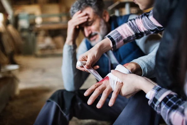 A woman bandaging a hand of a man worker after accident in carpentry workshop. — Stock Photo, Image