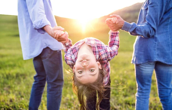 En liten flicka med hennes senior morföräldrar ha roligt utanför i naturen vid solnedgången. — Stockfoto