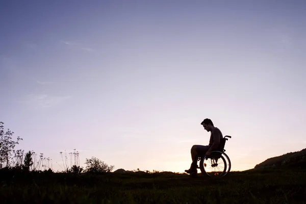 Un joven en silla de ruedas en la naturaleza por la noche . — Foto de Stock