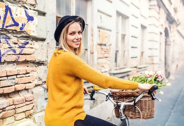 自転車と日当たりの良い春の町で花を持つ若い女性. — ストック写真