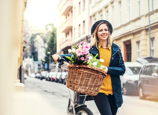 自転車と日当たりの良い春の町で花を持つ若い女性. — ストック写真