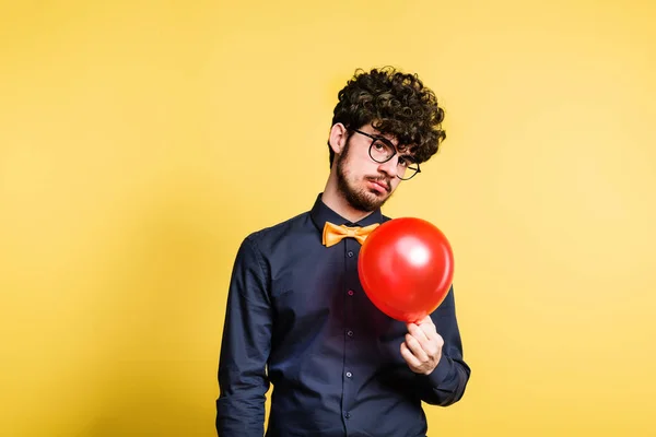 Portret van een jonge man met ballon in een studio op een gele achtergrond. — Stockfoto