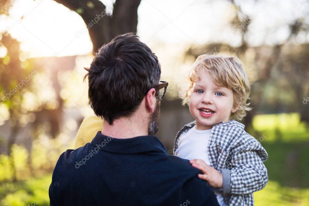 A father holding his toddler son outside in spring nature.