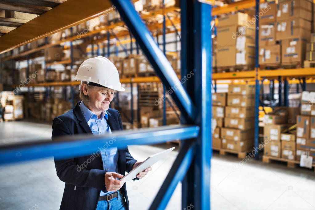 Senior woman warehouse manager or supervisor with tablet, working.