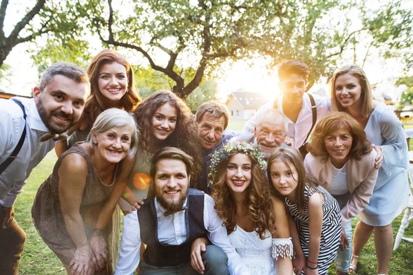 Bruid, bruidegom, gasten poseren voor de foto bij de bruiloft receptie buiten in de achtertuin. — Stockfoto