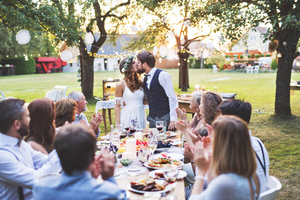 Bride and groom with guests at wedding reception outside in the backyard.