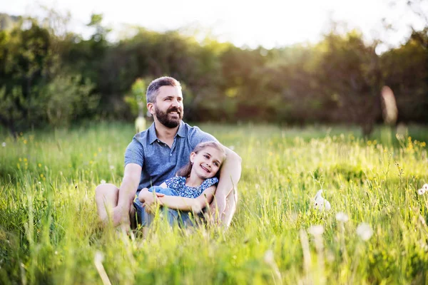 Otec s malou dcerou sedět na trávě v jarní přírodě. — Stock fotografie