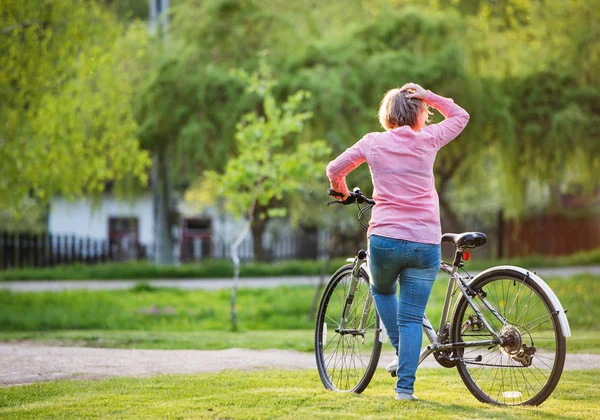 Seniorka s jízdním kolem venku v jarní přírodě. — Stock fotografie