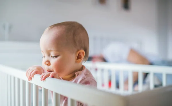 Una niña pequeña de pie en una cuna en el dormitorio en casa . —  Fotos de Stock