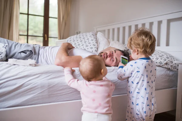 Smartphone ve babalarının yatak yatak odasında iki yürümeye başlayan çocuk. — Stok fotoğraf