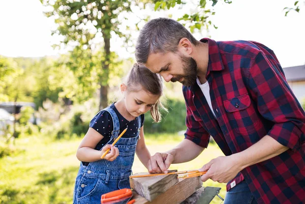 Padre con una pequeña hija afuera, haciendo pajarera de madera . — Foto de Stock