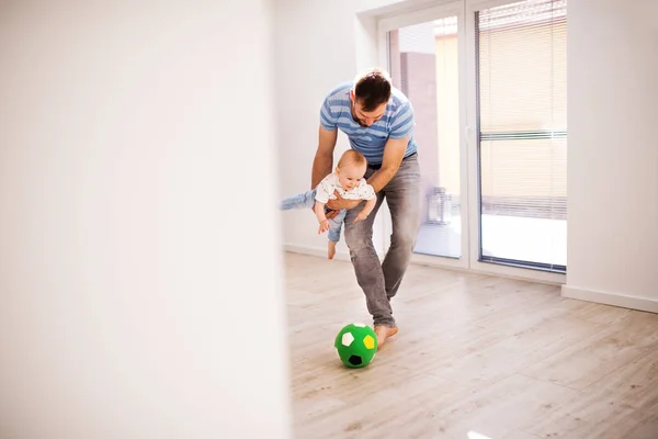 Jovem pai com um filho bebê em casa brincando com uma bola . — Fotografia de Stock
