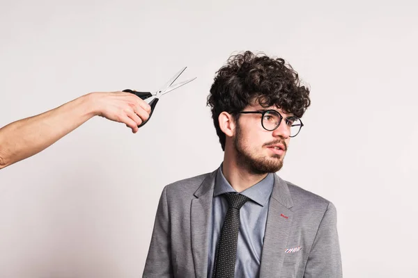 Portret van een jonge man in een studio en een hand met een schaar. — Stockfoto