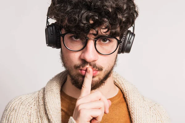 Porträtt av en ung man med hörlurar i en studio, finger på hans mun. — Stockfoto