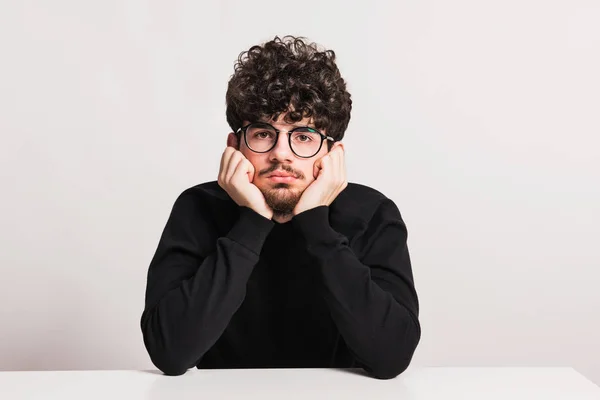 Joven hombre aburrido en un estudio, sentado a la mesa . —  Fotos de Stock