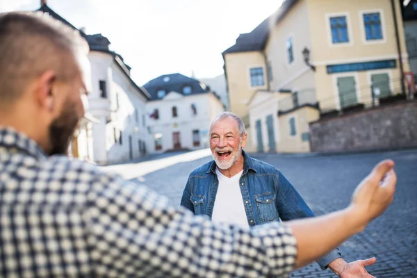 Un hijo hipster adulto y su padre jubiloso en la ciudad, saludando . —  Fotos de Stock