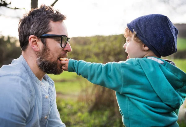 Ein kleiner Junge schenkt seinem Vater im Frühling draußen einen Keks. — Stockfoto